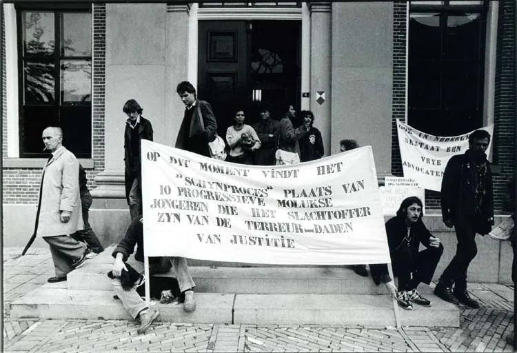 Twee bezoekers bij een fotowand in de tentoonstelling; de een filmt, de ander schrijft een aantekening bij een foto