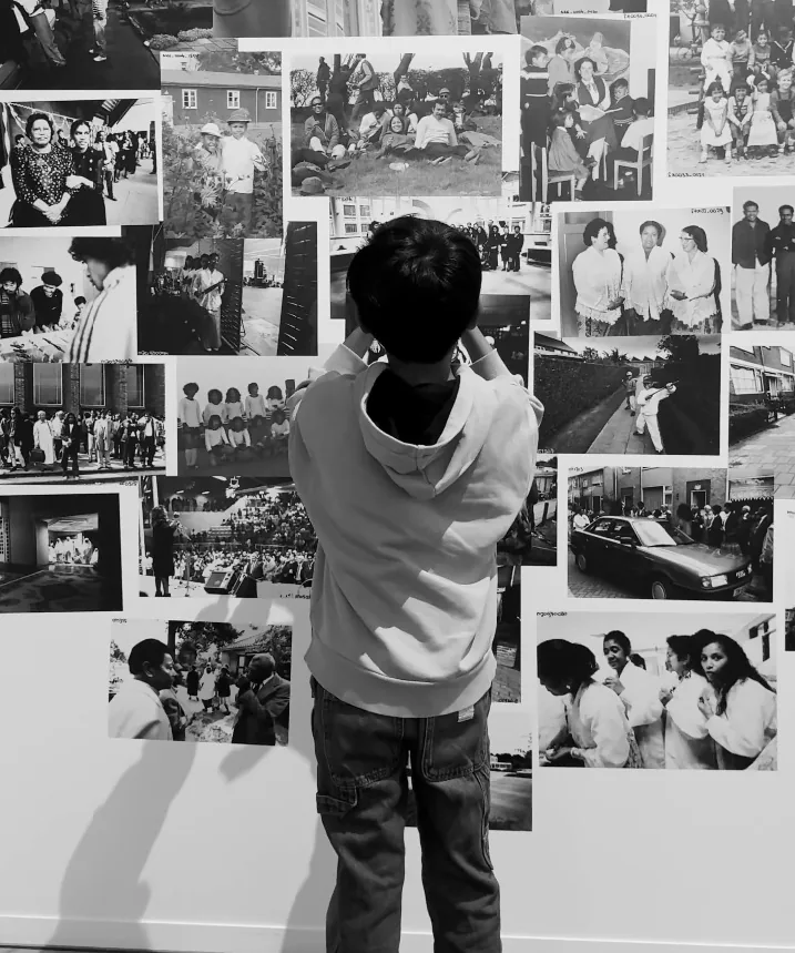 Een oudere bezoeker schrijft een herinnering bij een foto op de wand van de tentoonstelling